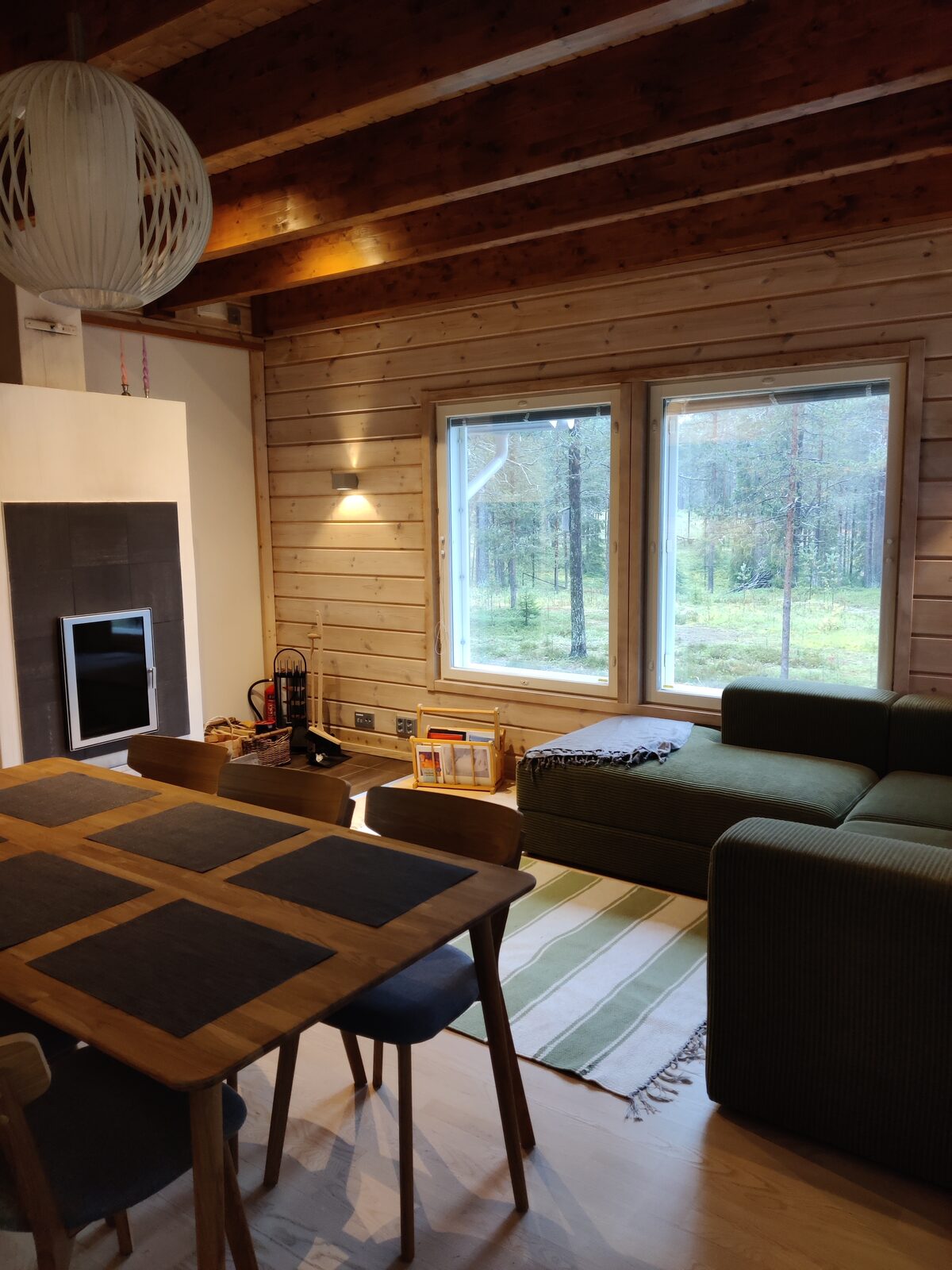 Wohnzimmer mit Kaminofen, grünem Sofa und Fenster zum Garten